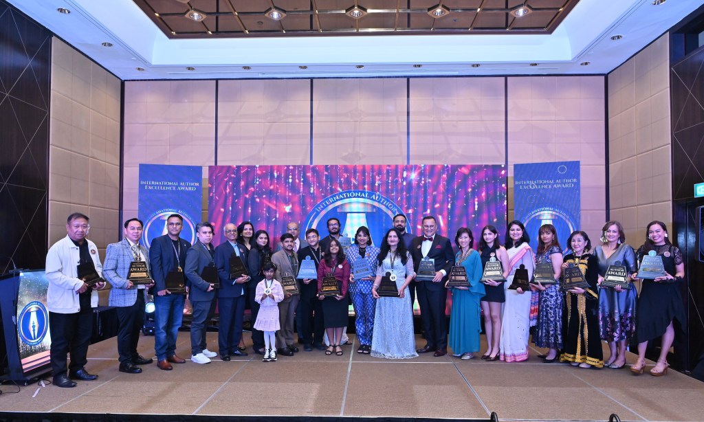 Group of award recipients posing in formal attire at the International Author Excellence Award ceremony, featuring a backdrop of colourful lights and banners.